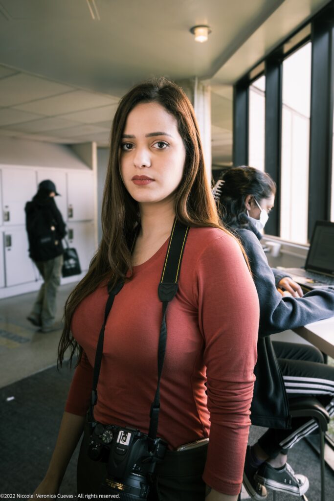 beautiful lady wearing an orange and a dslr on her neck, staring at camera.