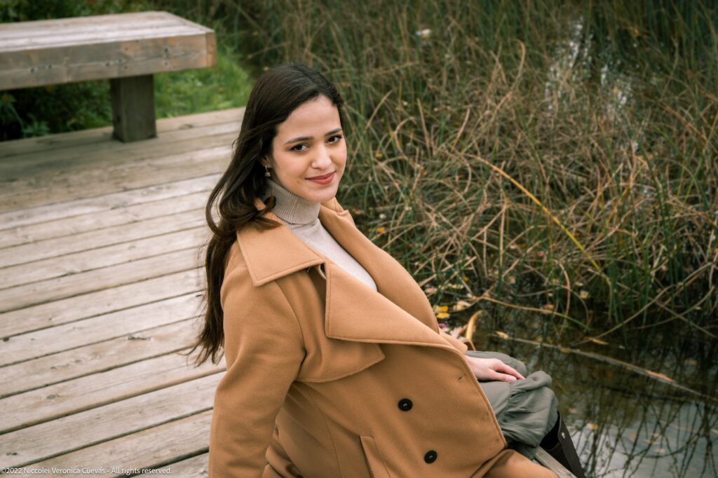 outdoor shot of beautiful lady wearing a brown coat smiling for the camera.